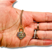 Gold chain with a multicolored padlock pendant held in a hand.
