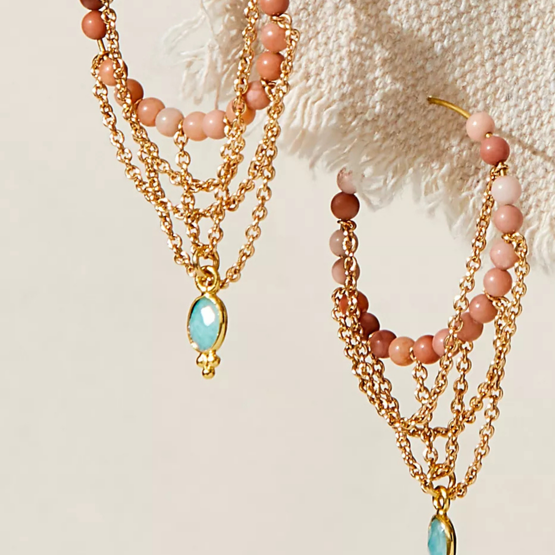 Jewelry set with gold chains, pink beads, and a turquoise pendant on a textured beige background.
