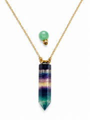 A gold chain necklace featuring a vertical point pendant made of a striped gemstone in shades of teal, green, purple, and blue, with a separate round green bead and small gold cap above it, shown on a white background.