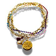 Stack of gold and beaded bracelets with a quote charm on a white background