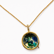 A gold chain necklace with a round pendant containing colorful raw gemstone chips in shades of blue, green, and yellow, set in a gold bezel on a white background.