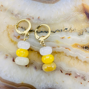 Gold hoop earrings with yellow and white beads on a marble surface