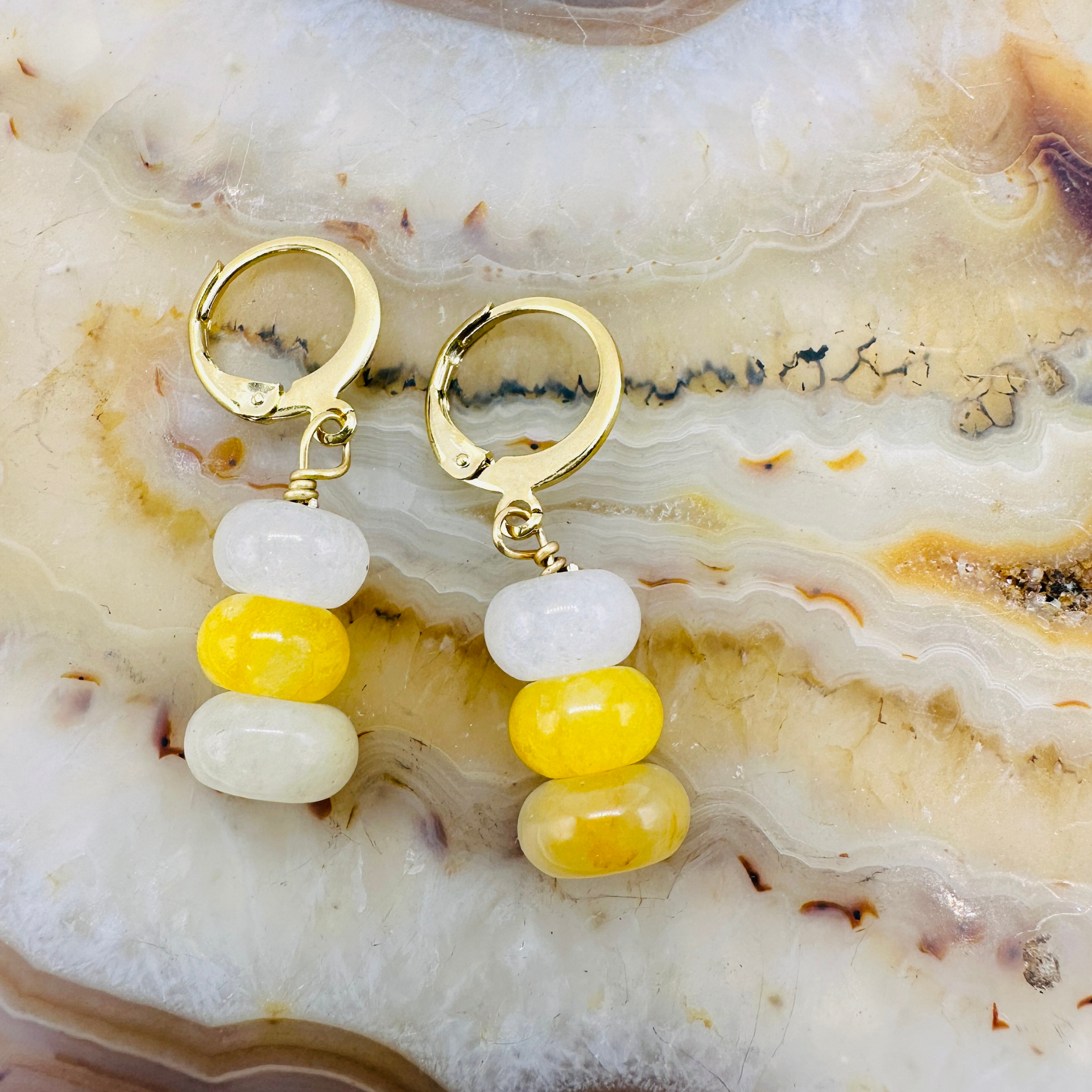 Gold hoop earrings with yellow and white beads on a marble surface