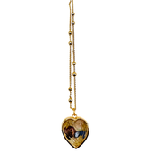 A gold heart-shaped pendant necklace featuring a detailed religious illustration of Saint Christopher carrying the Christ Child, suspended from a delicate gold beaded chain against a plain white background.