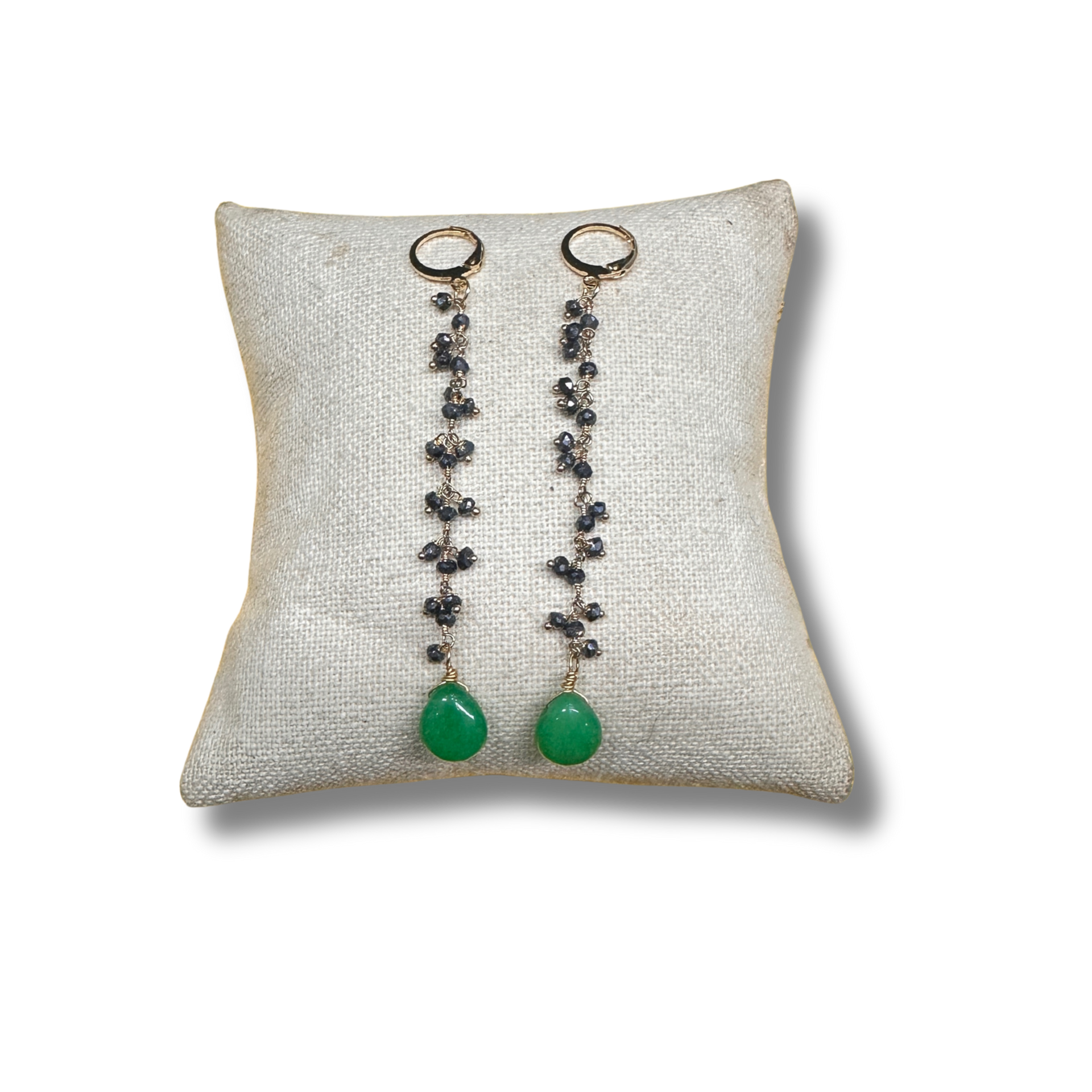 Pair of earrings with green beads on a textured pillow against a white background