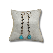 Pair of earrings with turquoise stones on a textured pillow against a white background