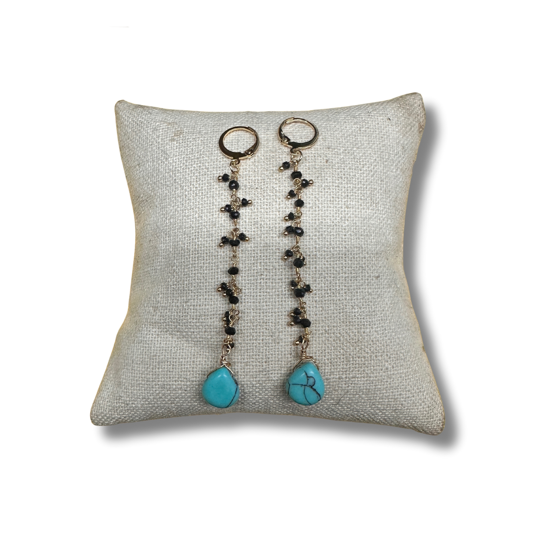 Pair of earrings with turquoise stones on a textured pillow against a white background