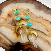 Gold earrings with turquoise beads and clear crystals on a decorative stone surface