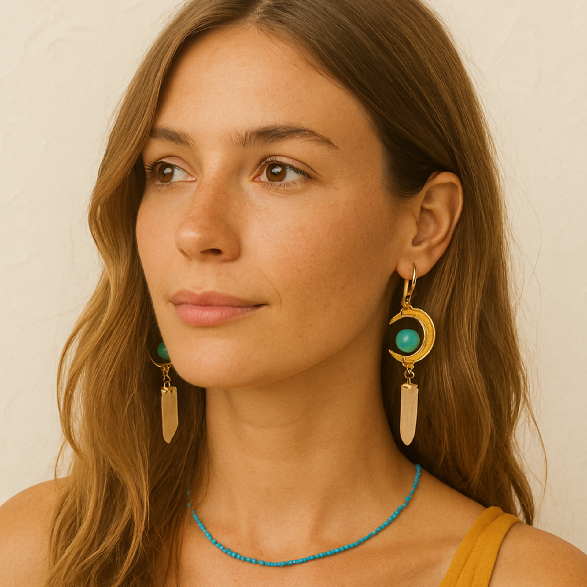 Woman wearing gold earrings with turquoise stones against a neutral background