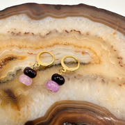 Gold hoop earrings with pink and black beads on a decorative stone surface