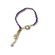 Purple beaded bracelet with gold accents and pearl charm on a white background