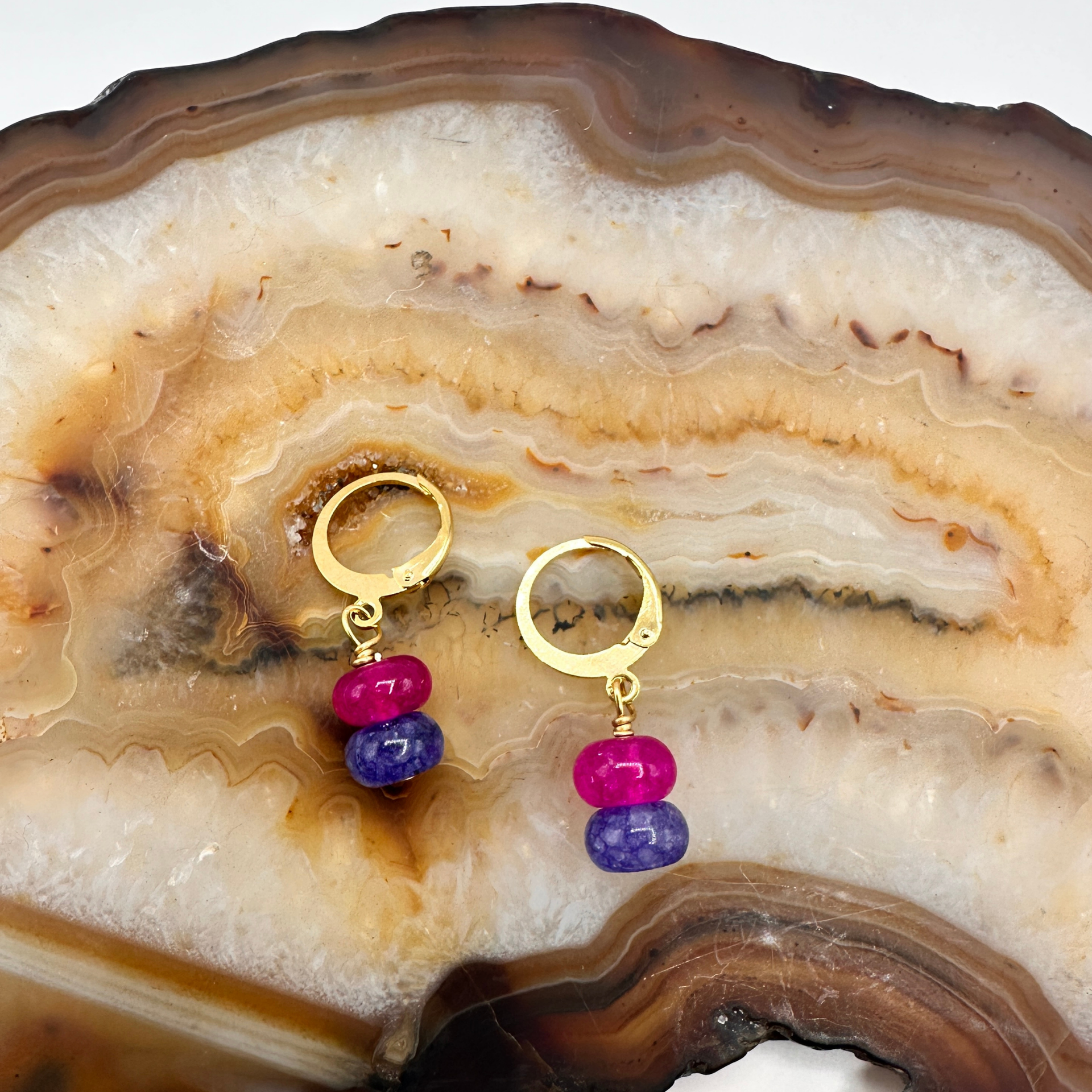 Gold earrings with pink and blue beads on a decorative stone surface
