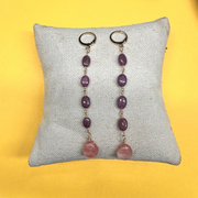 Pair of earrings with purple and pink beads on a gray pillow against a yellow background