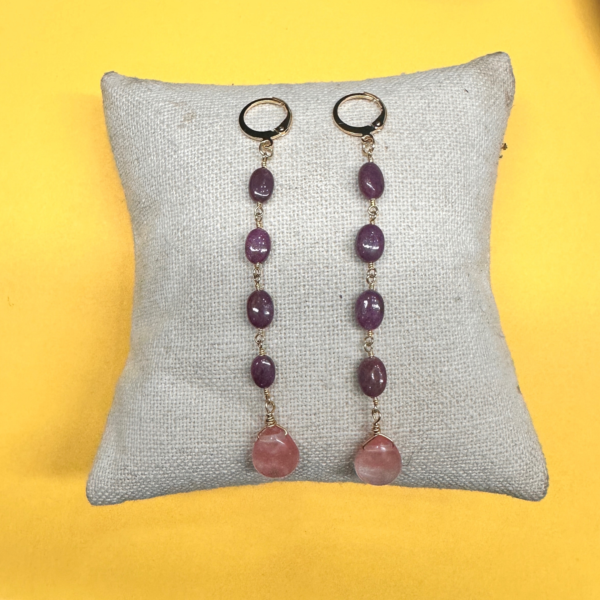 Pair of earrings with purple and pink beads on a gray pillow against a yellow background