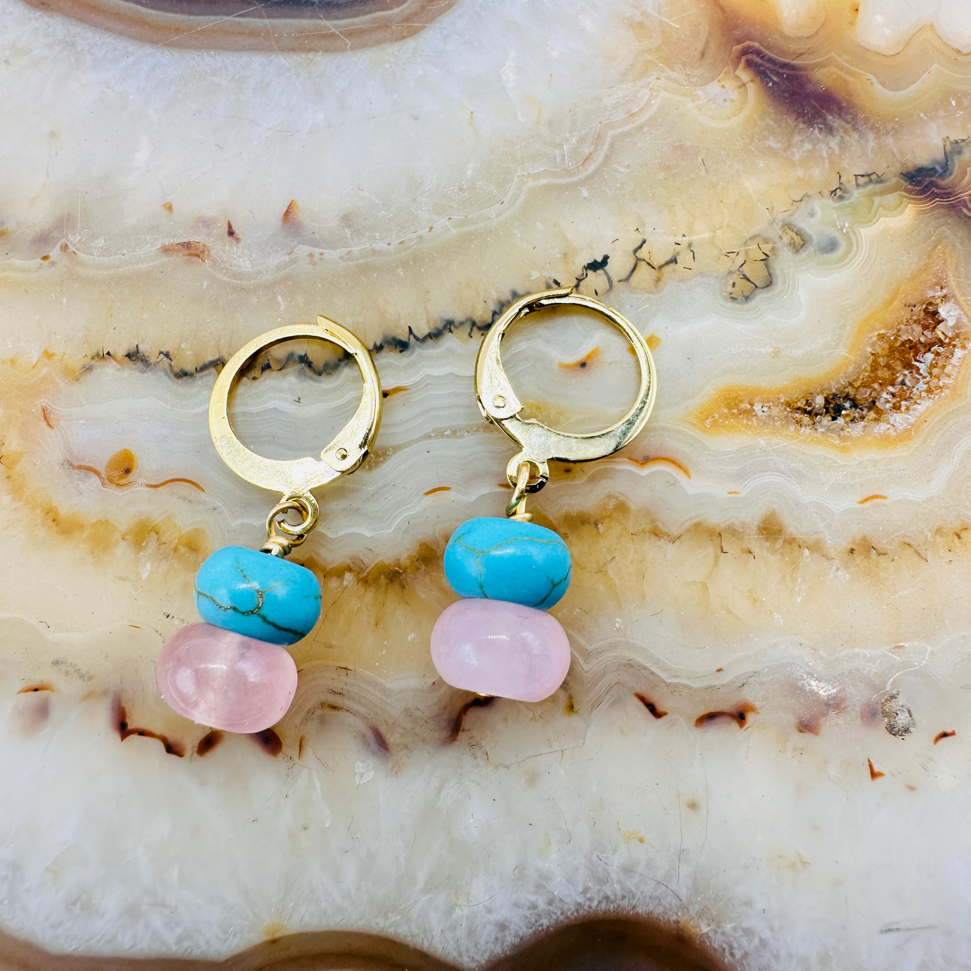 Gold hoop earrings with turquoise and pink beads on a marble surface