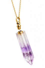 A gold chain necklace featuring a clear quartz point pendant with natural purple and lavender inclusions, suspended against a solid white background.