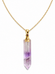 A gold chain necklace featuring a clear quartz point pendant with natural purple and white inclusions, accented by a small round red gemstone at the bail.