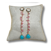 Pair of earrings with pink beads and turquoise stones on a textured pillow