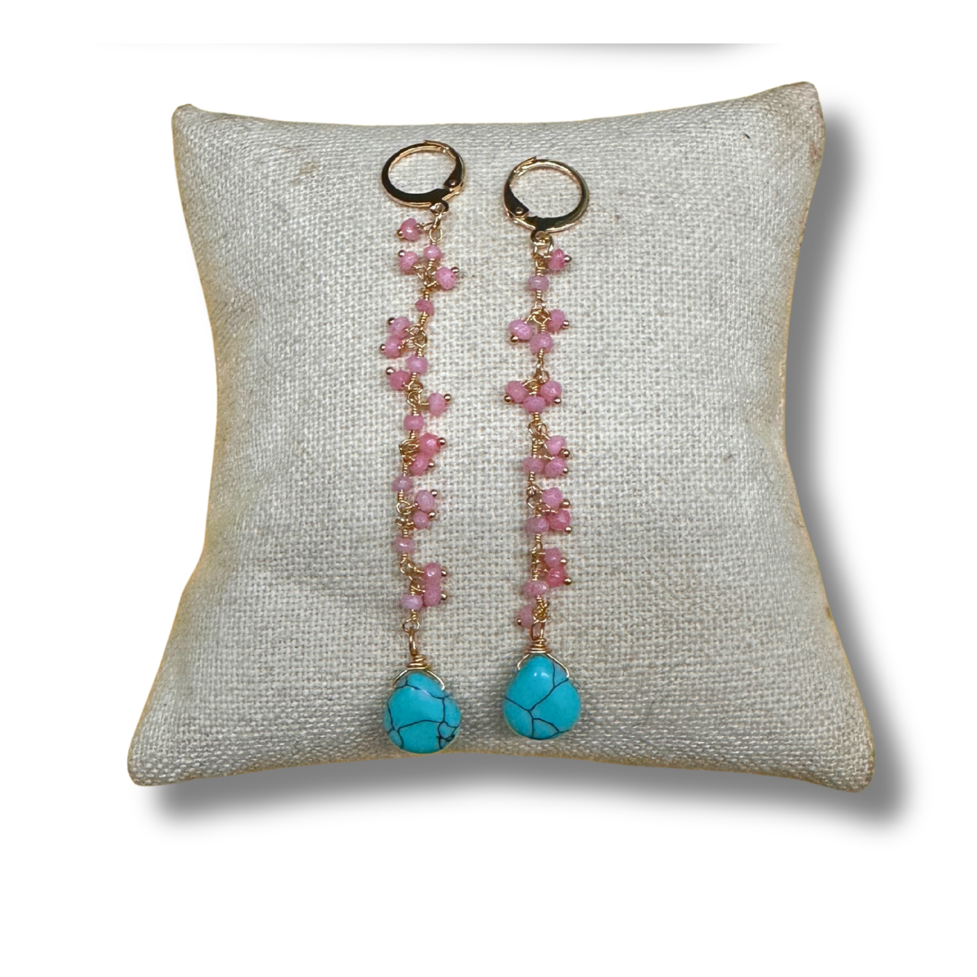 Pair of earrings with pink beads and turquoise stones on a textured pillow
