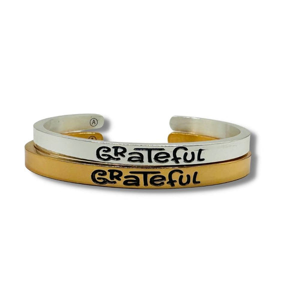 Two Alisa Michelle bracelets with Grateful Engraved. One is gold and the other is silver.